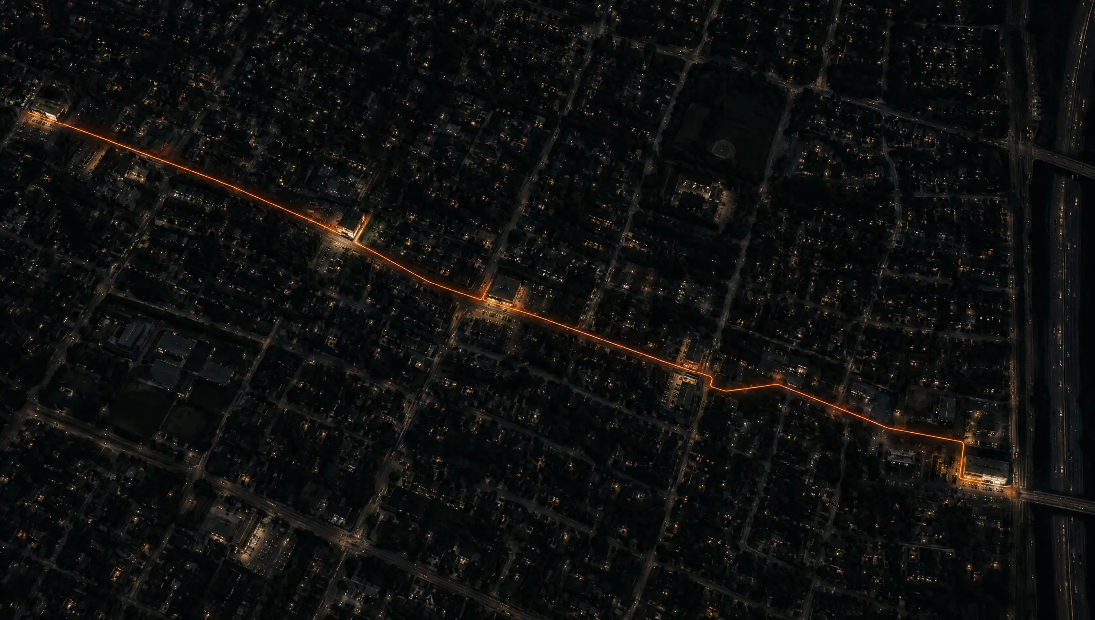 Night aerial of a city grid with a single orange line routed between storefronts